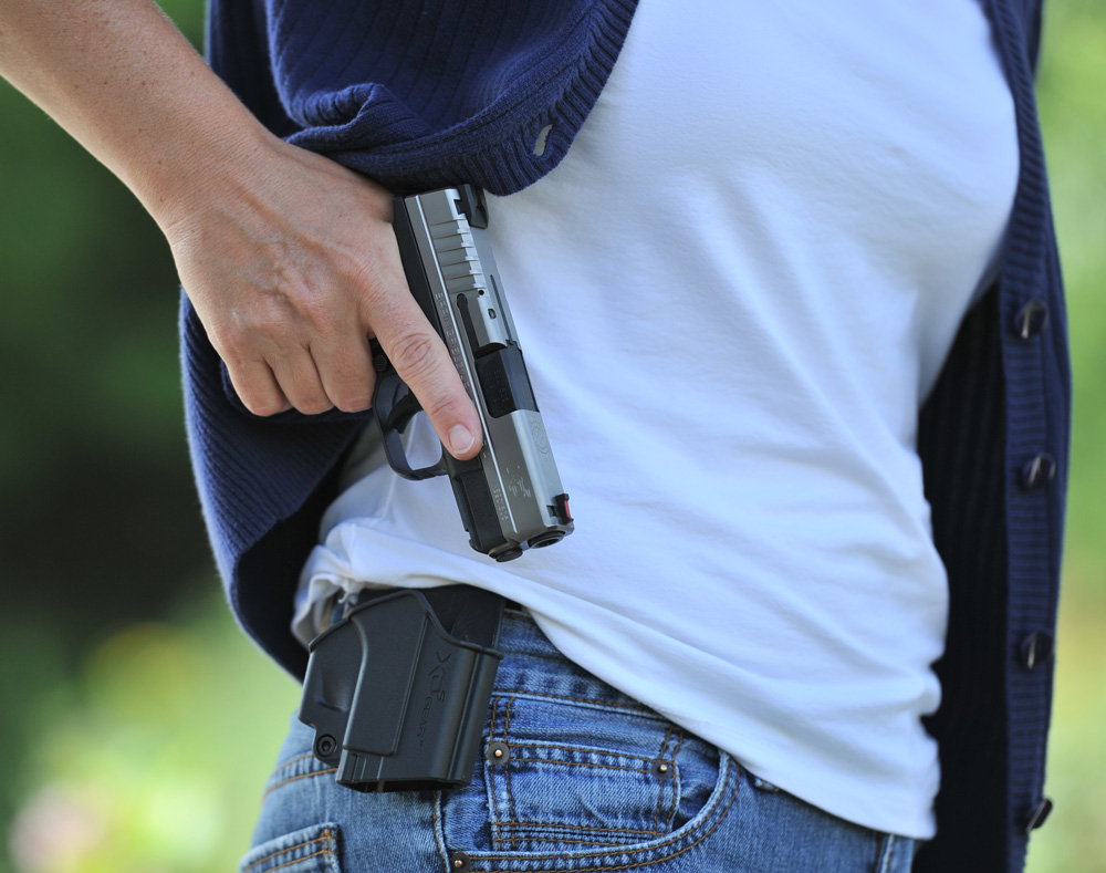 close-up photo of a woman taking off her handgun from the holster attached in her hips