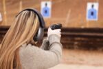 a woman wearing ear muffs and holding up a handgun to the target